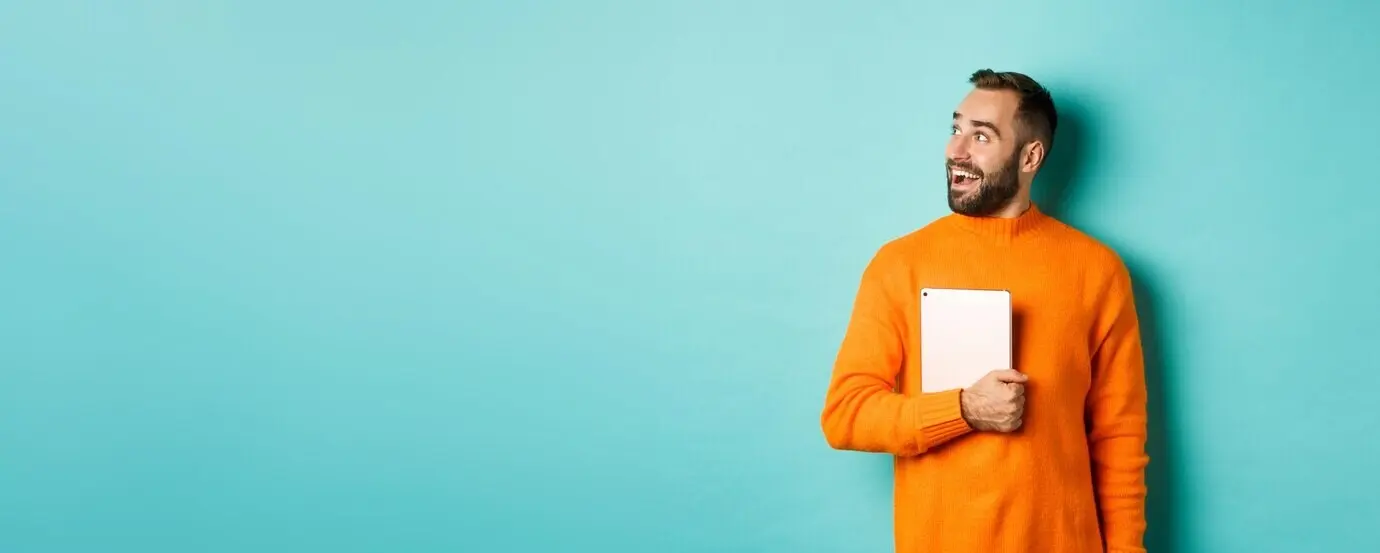 Gutaussehender Mann hält einen Laptop, blickt mit Überraschung und Staunen nach links und steht in einem orangefarbenen Pullover.